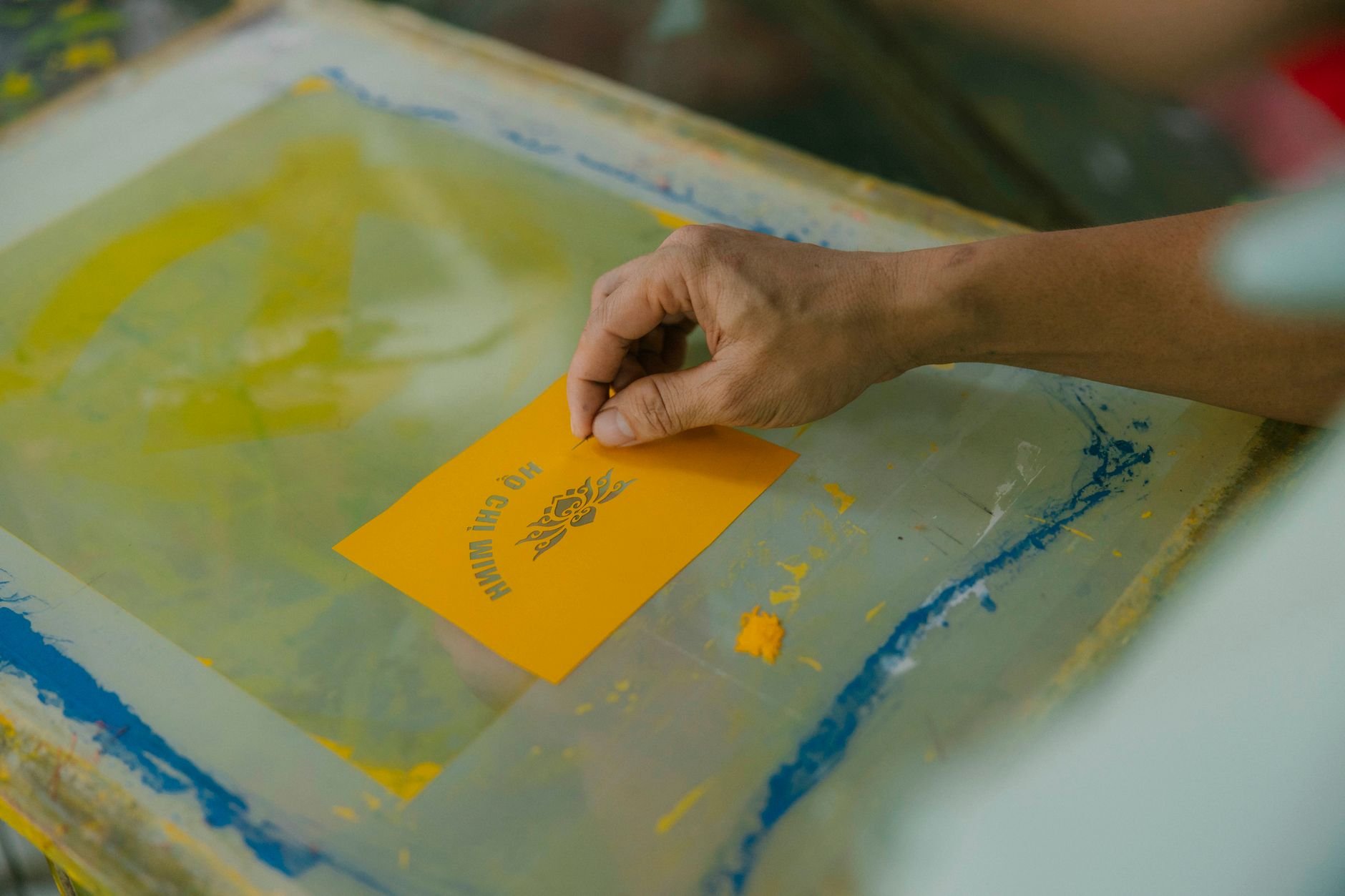A detailed look at a hand screen printing, focusing on a yellow card with design.